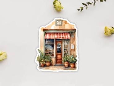 Sticker eines kleinen Geschäfts mit rotem und weiß gestreiftem Markisen, einer Uhr über dem Eingang und zwei großen Pflanzgefäßen vor der Tür. Die Fassade hat warme Farbtöne und lädt zum Einkaufen ein.
